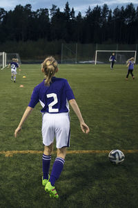 Rear view of girl playing with soccer ball on field