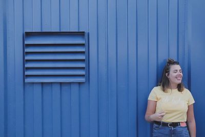 Smiling young woman standing against blue wall