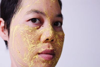 Close-up portrait of woman applying facial mask against wall