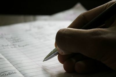 Cropped hand of person writing on book with pen