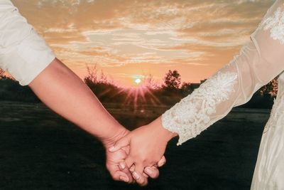 Midsection of couple kissing against sky during sunset