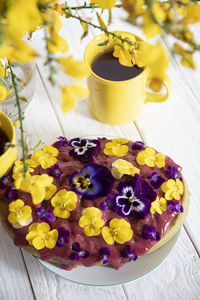 Delicious cake decorated with yellow purple pansy flowers on white wooden table