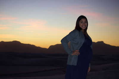 Portrait of smiling young woman standing against sky during sunset