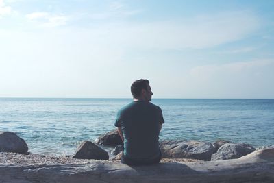 Rear view of man sitting on rock against sea