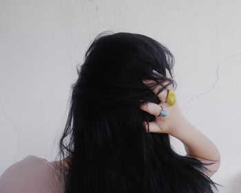Rear view of woman with hand in hair against wall