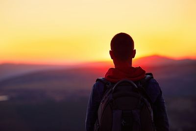 Rear view of man standing against orange sky