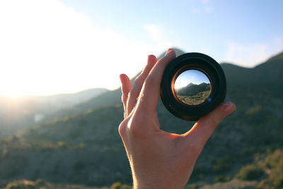 Close-up of hand holding camera lens against sky