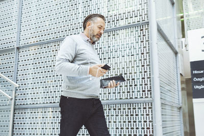 Businessman with digital tablet listening music though mobile phone while walking in office