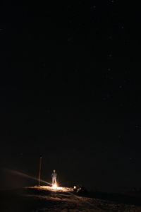 Silhouette people standing by illuminated bonfire against sky at night