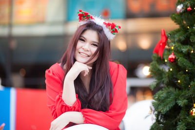 Portrait of smiling woman sitting by christmas tree