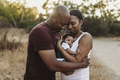 Close up happy mother and father cuddling infant girl backlit field