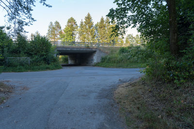 Bridge over road by trees against sky