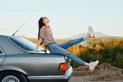 Side view of woman sitting on road against clear sky