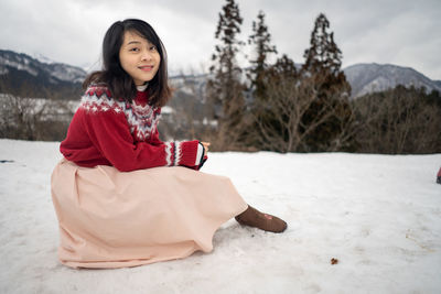 Portrait of smiling woman sitting on snow covered land
