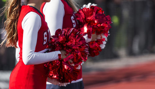 Two high school cheerleaders pompoms are watching the football game ready to cheer for their team.