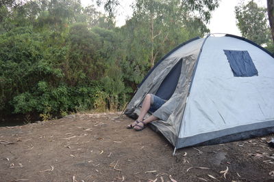 Low section of person sitting at tent against sky