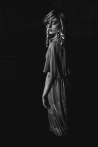 Young woman with eyes closed standing against black background