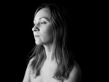 Portrait of young woman looking away against black background