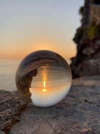 Close-up of crystal ball on rock at beach against sky during sunset