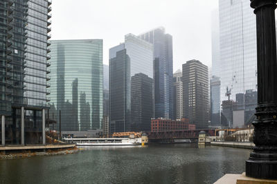 Modern buildings by river against sky in city