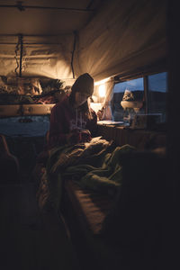 Woman reading book while sitting in camper van during sunset