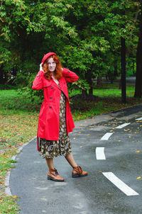 Young happy woman with red hair, freckles, beret, coat walking in autumn park, drinking coffee