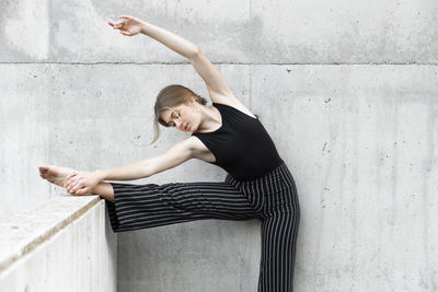 Dancer in black striped pants stretching in front of concrete wall