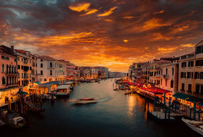 Boats in canal amidst buildings against sky during sunset