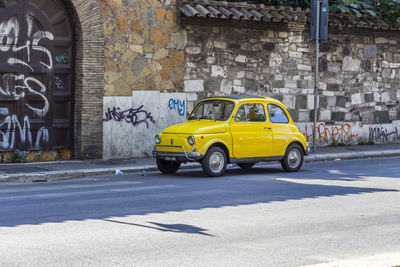 Yellow car on street against wall