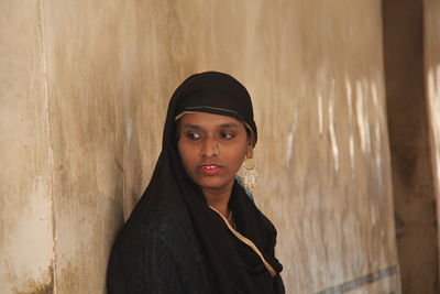 Portrait of young woman standing against wall