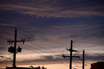 Low angle view of silhouette electricity pylon against dramatic sky