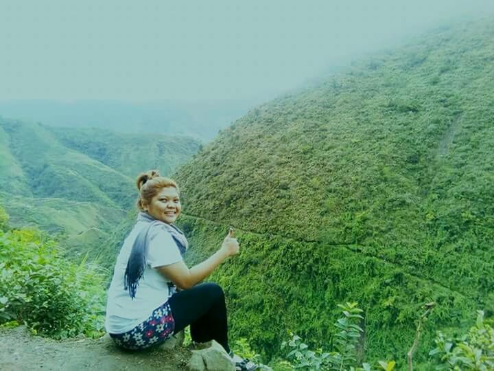 WOMAN SITTING ON MOUNTAIN AGAINST SKY