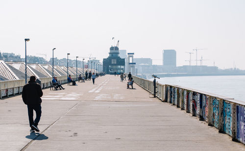 Rear view of people walking on promenade against clear sky