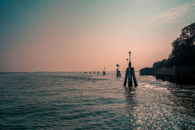 Silhouette people standing on sea against sky during sunset