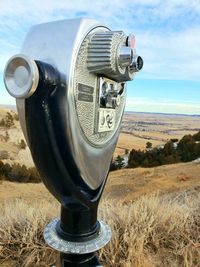 Close-up of coin-operated binoculars on field against sky