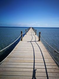 Wooden pier over sea against blue sky