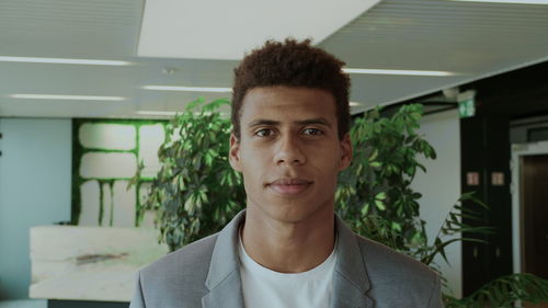 Portrait of young businessman standing at corridor indoors