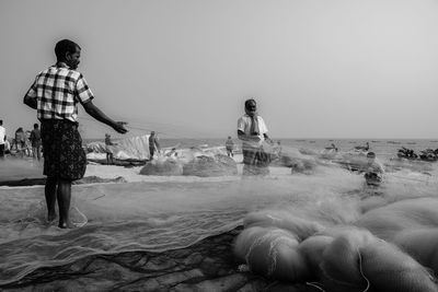 Rear view of people standing on beach against clear sky