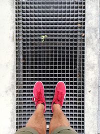 Low section of man wearing red shoe standing on sewer
