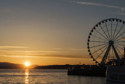 Silhouette ferris wheel by sea against sky during sunset