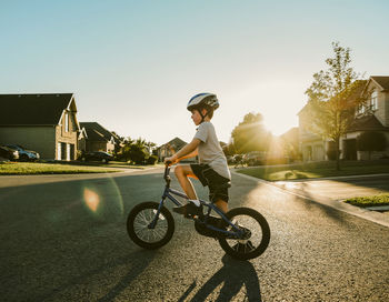 Side view of boy riding bicycle on road against clear sky during sunset