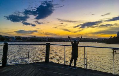 Silhouette man standing by railing against sky during sunset