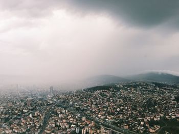 Aerial view of cityscape against cloudy sky