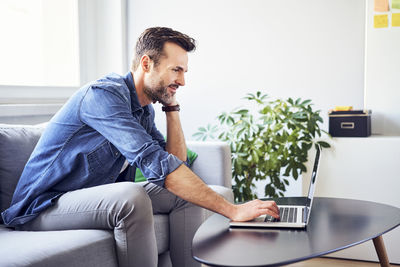 Smiling man sitting on sofa using laptop