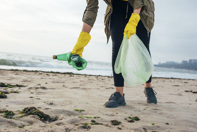 Environmentalist with garbage bag cleaning beach while standing against clear sky