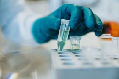 Woman wearing protective glove holding test tube while standing at laboratory