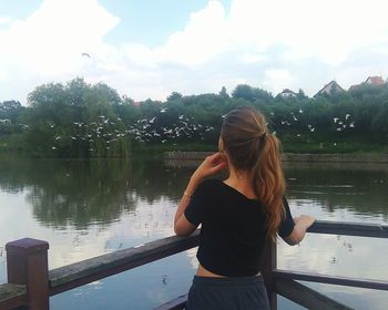 Rear view of woman standing by lake against sky