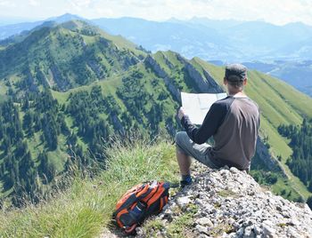 Man reading map while sitting against mountains