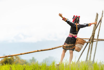 Rear view of woman with arms outstretched on field against sky