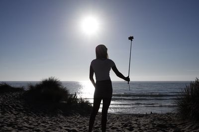 Rear view of woman taking selfie at beach against sky